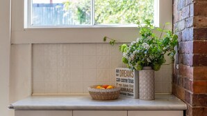 A kitchen counter with a window, a potted plant, a basket of fruit, and a motivational quote sign. - Hollybrooke Cottage, prestige suburb in Launceston (East Launceston)