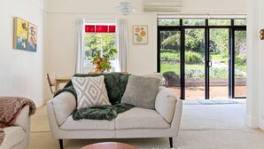A living room with a sofa, a coffee table, and a view of a garden through large glass doors. - Hollybrooke Cottage, prestige suburb in Launceston (East Launceston)