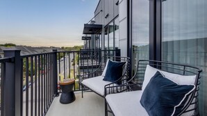 A balcony with two chairs and a small table, overlooking a street with cars and buildings. - Chic Midtown Penthouse Escape - Pool, Gym, Patio with City Views (Nashville)
