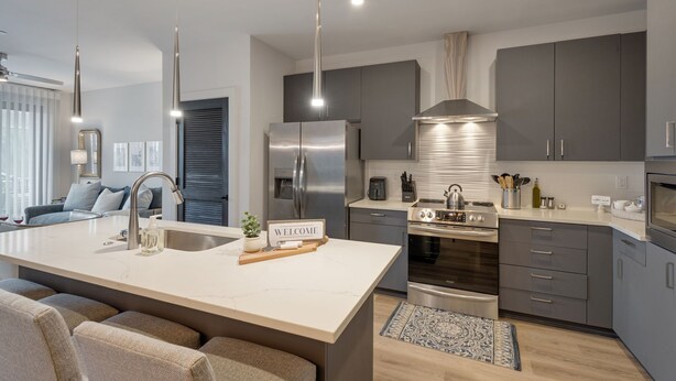 A modern kitchen with a central island, stainless steel appliances, and a "WELCOME" sign. - Chic Midtown Penthouse Escape - Pool, Gym, Patio with City Views (Nashville)