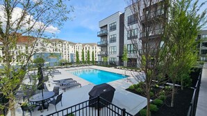 A modern apartment complex with a swimming pool, outdoor seating, and a view of surrounding buildings. - Chic Midtown Penthouse Escape - Pool, Gym, Patio with City Views (Nashville)