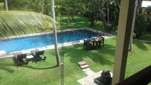A swimming pool with lounge chairs and a table, surrounded by well-maintained grass and palm trees.