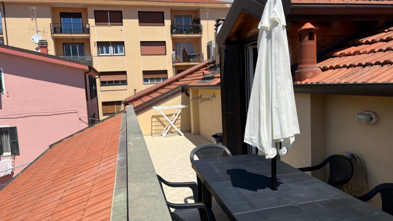 A balcony with a tiled roof, a table, chairs, and a white umbrella.