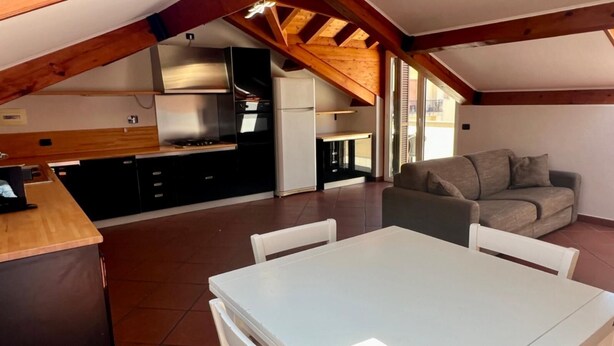 Amplia sala de estar con una mesa y sillas de comedor, un sofá y una cocina equipada con electrodomésticos modernos.