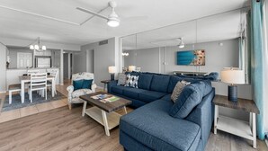 A modern living room with a blue sofa, a coffee table, and a dining area with white chairs and a table. - NEW RENTAL! COMPLETELY RENOVATED! GREAT BEACH AND POOL VIEWS (Panama City)
