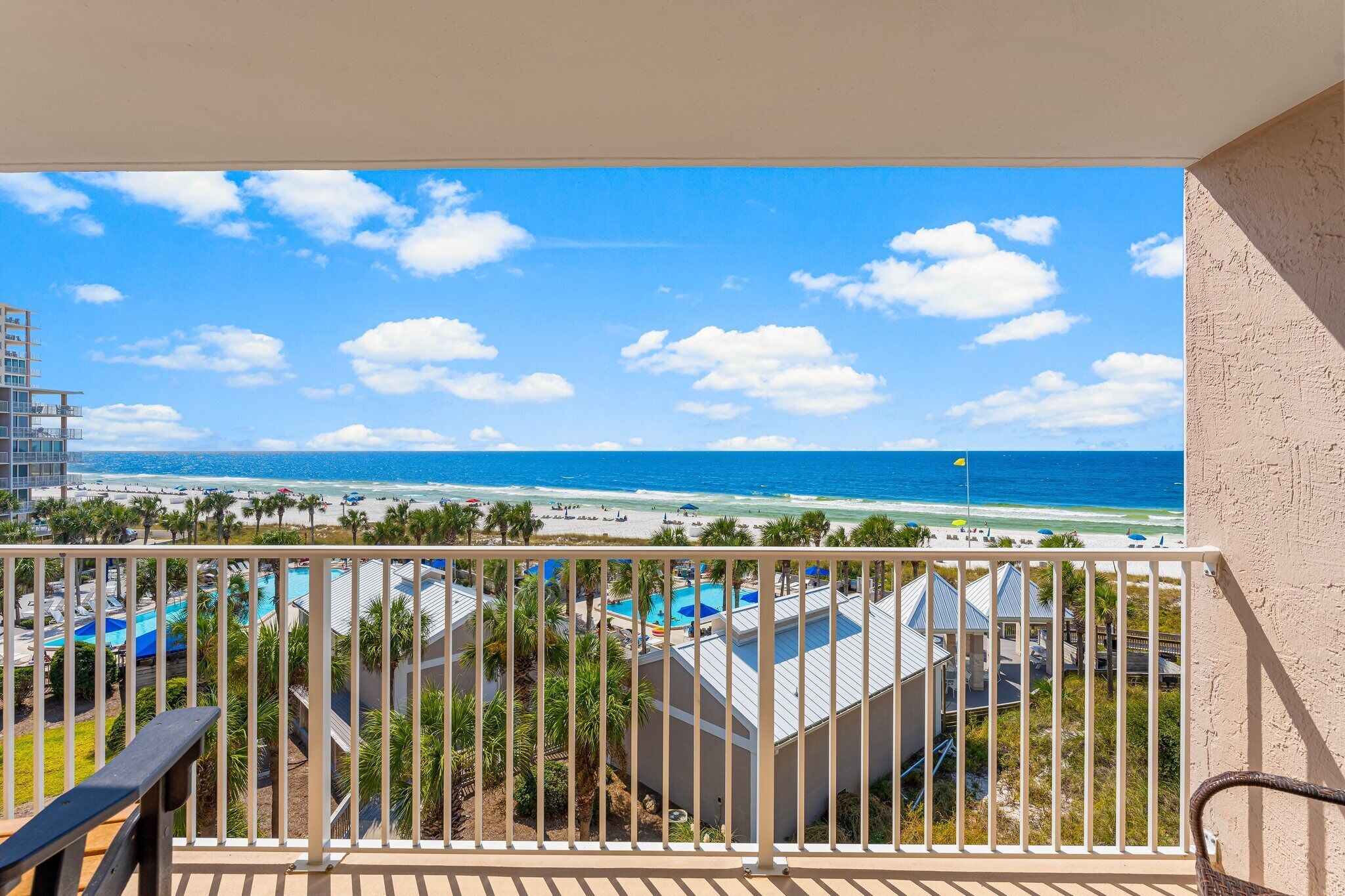 A balcony with a view of a beach, pool area, and resort buildings.