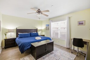Un dormitorio con cama, mesitas de noche, escritorio, silla, ventilador de techo y ventana con persianas.