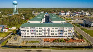 Un hotel de varios pisos con techo verde, varios balcones y una torre de agua al fondo.