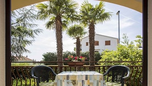 Eine Terrasse mit Tisch und zwei Stühlen, umgeben von einem Metallgeländer und Palmen.