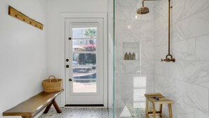 Un baño con cabina de ducha de vidrio, un banco y una puerta con vistas al exterior.