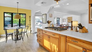 Una cocina con una isla central, armarios de madera y un comedor con sillas.