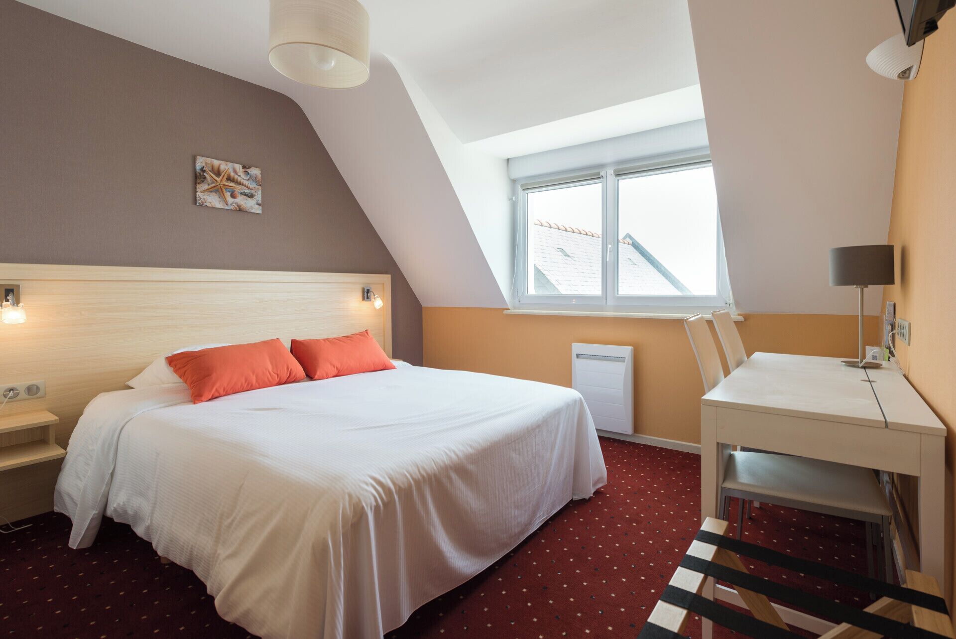 Habitació d'hotel amb llit, escriptori, cadira, radiador, finestra i llum al sostre.