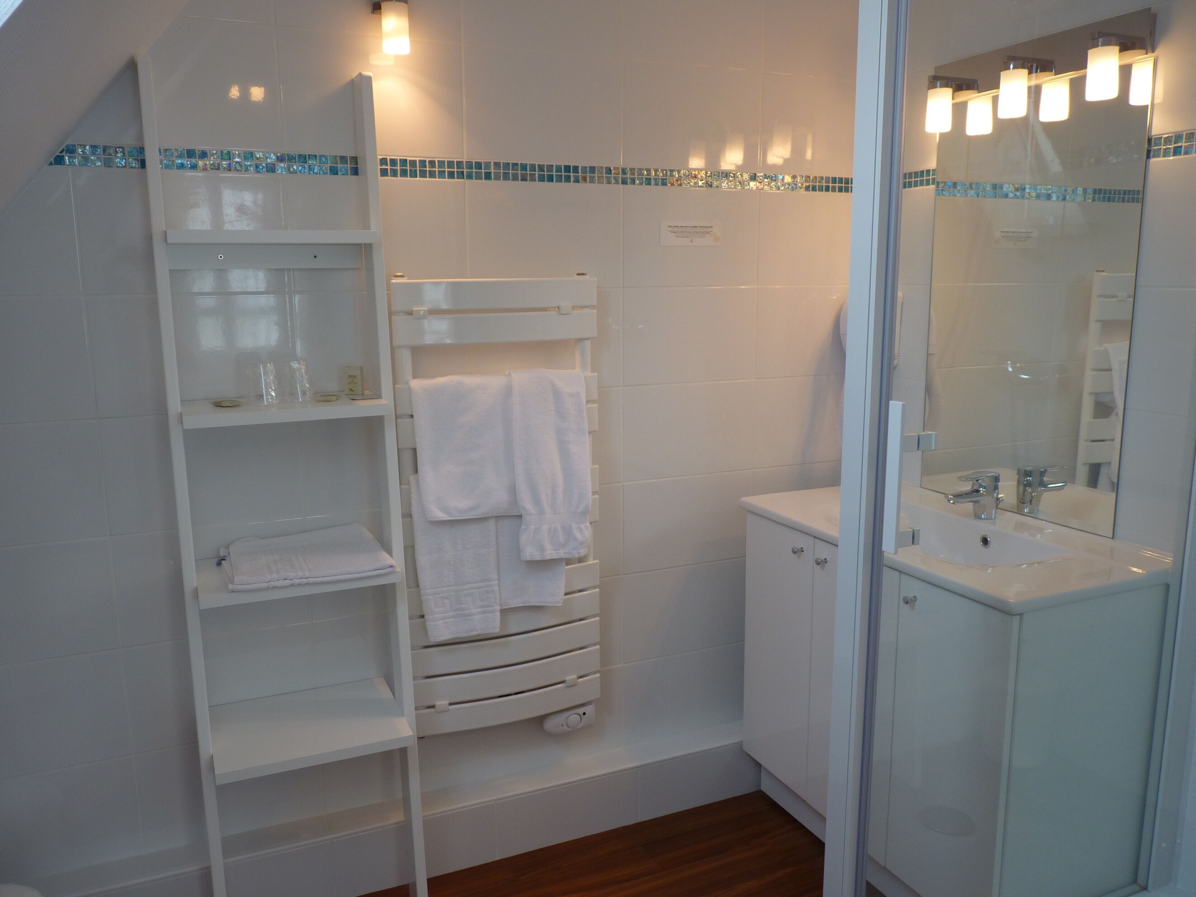 Een moderne badkamer met een wit wastafelmeubel, een douchecabine met glazen wanden en een houten vloer.