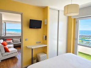 A bedroom with a bed, a TV, a sofa, and a view of the ocean.