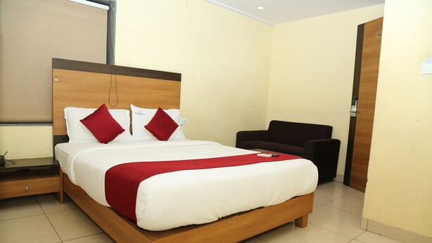 A neatly made bed with a wooden frame, two red pillows, and a white comforter. - Sri Brundavan Grand Inn (Anakapalle)