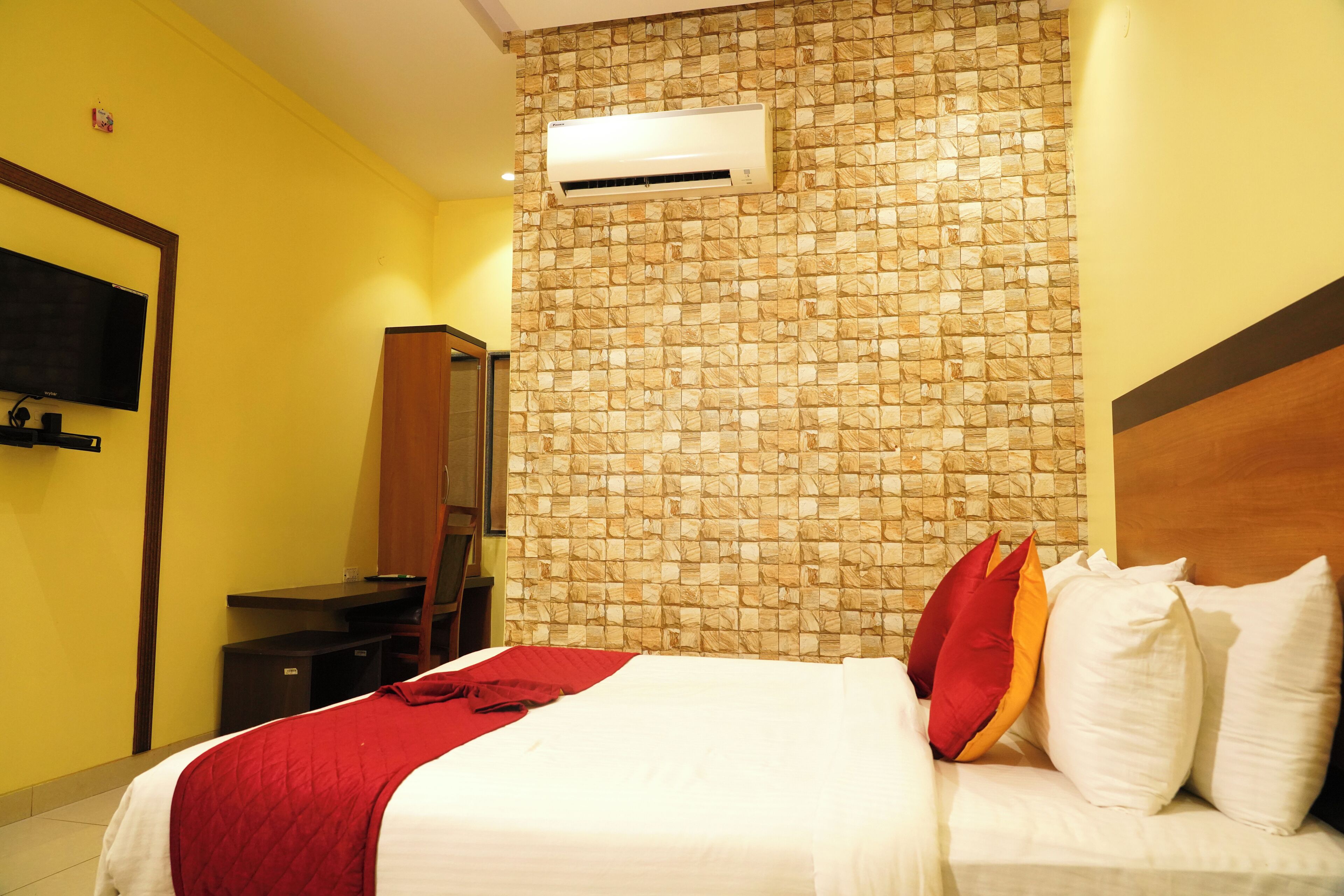 Habitación de hotel con cama, televisor montado en la pared, aire acondicionado y espejo.