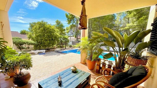 Eine Terrassenanlage im Freien mit Pool, Topfpflanzen, Korbmöbeln und einem kleinen Tisch mit einer Dekoration.