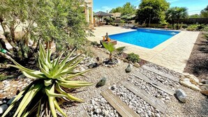 Ein Schwimmbecken, umgeben von einem angelegten Garten mit verschiedenen Pflanzen und einem Pavillon.