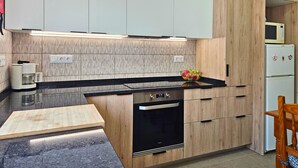 A modern kitchen with a black countertop, wooden cabinets, a Bosch refrigerator, and a microwave. - Retiro do Sol - Charming apartment in Lagos (Lagos)