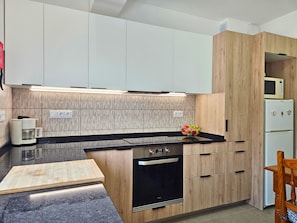 Een moderne keuken met een zwart aanrecht, houten kastjes, een Bosch koelkast en een magnetron.