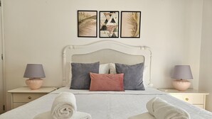 A neatly made bed with pillows, two bedside tables with lamps, and three framed artworks on the wall. - Retiro do Sol - Charming apartment in Lagos (Lagos)