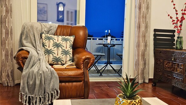 A living room with a brown leather chair, a table with a plant, and a view of the night sky. - Retiro do Sol - Charming apartment in Lagos (Lagos)