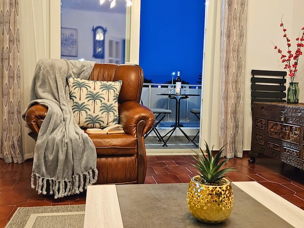 Un salon avec un fauteuil en cuir marron, une table sur laquelle est posée une plante, et une vue sur le ciel nocturne.