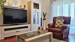 A living room with a TV, a brown leather sofa, a coffee table, and a bookshelf. - Retiro do Sol - Charming apartment in Lagos (Lagos)