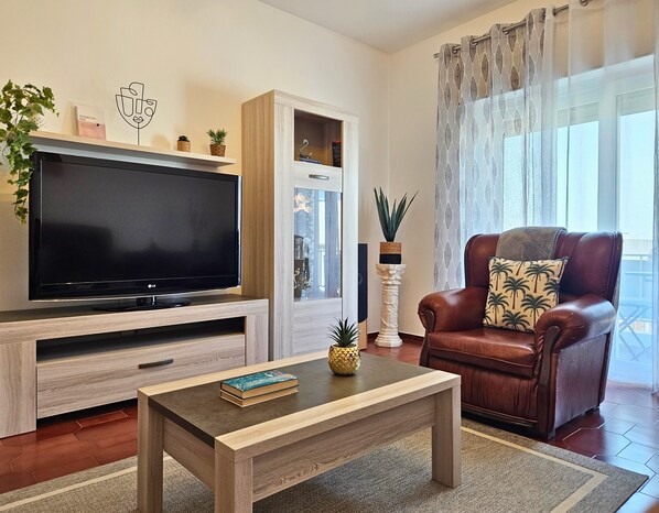 A living room with a TV, a brown leather sofa, a coffee table, and a bookshelf.