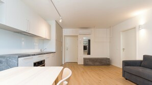 A modern kitchen with white cabinets, a marble countertop, and a dining area with a wooden table and chairs.
