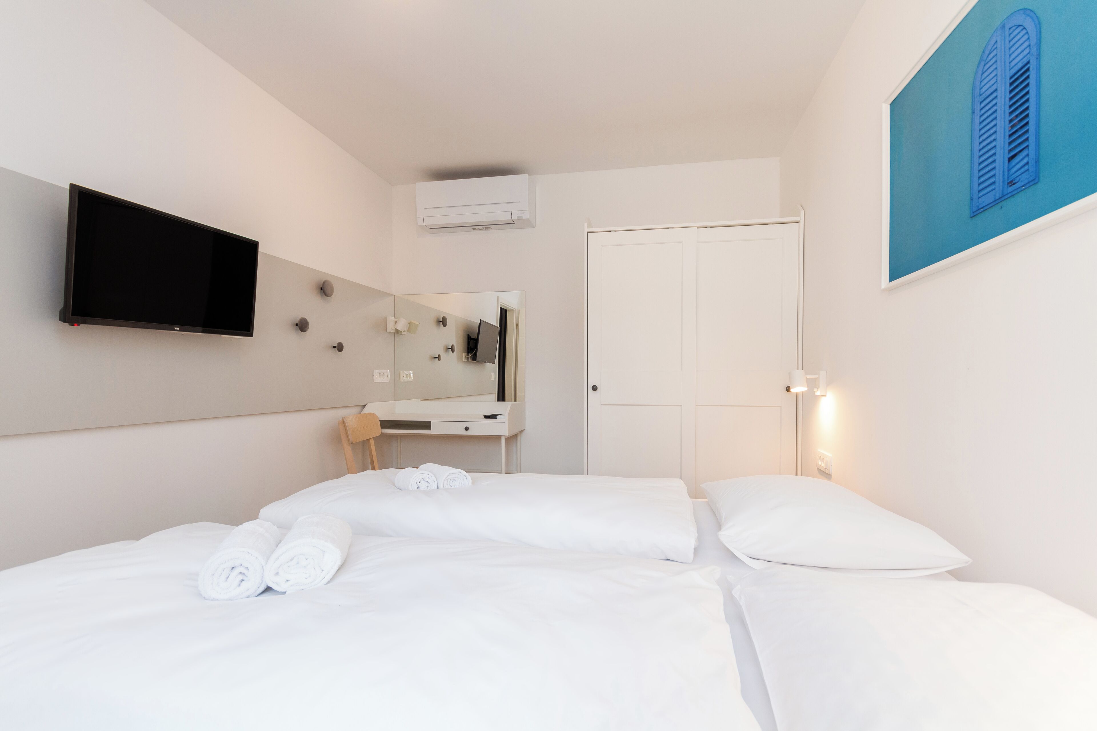 Una camera d'albergo con un letto, una TV a schermo piatto, uno specchio, un armadio e un quadro appeso al muro.