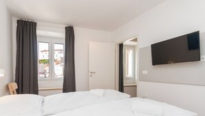 A hotel room with a large bed, a TV mounted on the wall, and a window with curtains.