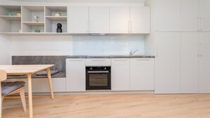 A modern kitchen with white cabinets, a built-in oven, and a dining area with a wooden table and bench.
