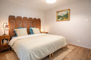 Ein Schlafzimmer mit Bett, Nachttisch, Lampe, Bücherregal und einem Bild an der Wand.