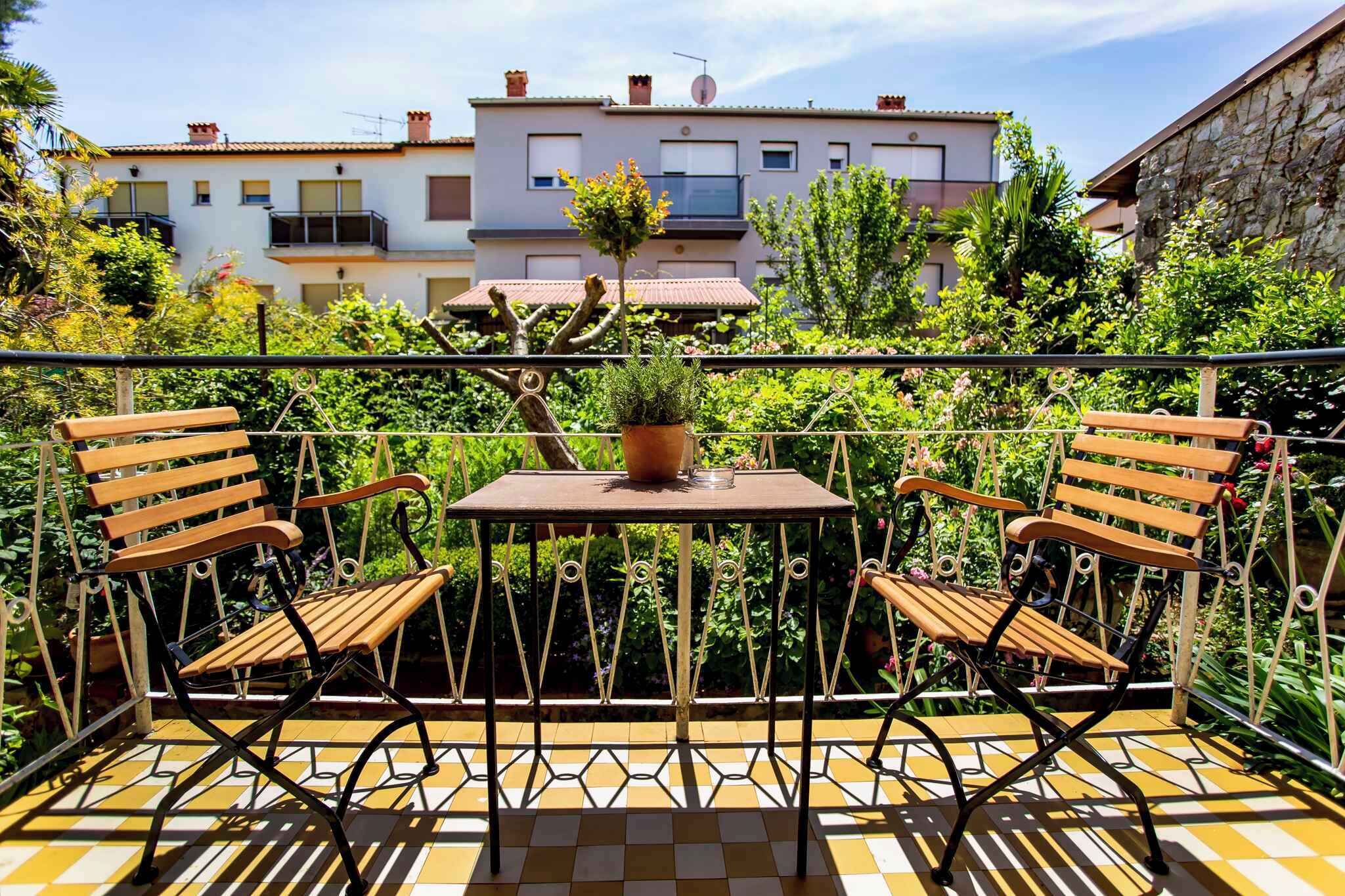 A balcony with two wooden chairs and a small table, surrounded by a metal railing and potted plants.