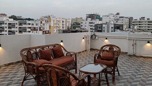 Une terrasse sur le toit, dotée de meubles en osier et d’un sol carrelé, offrant une vue panoramique sur la ville et ses différents bâtiments.
