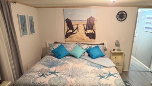 Un dormitorio con cama, dos almohadas, una mesita de noche, un reloj y obras de arte en la pared.