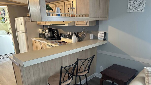 Una cocina con una isla central, dos taburetes de bar, una mesa de madera y un sofá marrón oscuro.
