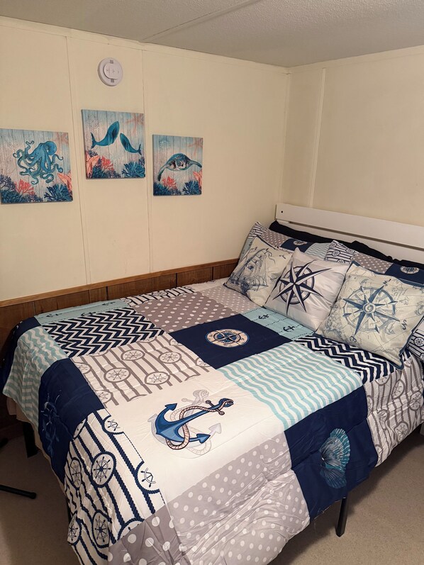 Una cama con colcha de temática náutica, cabecera de madera y tres cuadros colgados en la pared.