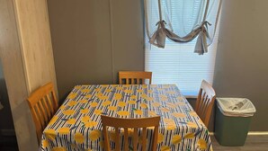 Un comedor con una mesa cubierta por un mantel amarillo y azul con motivos de hojas, rodeada de sillas de madera.