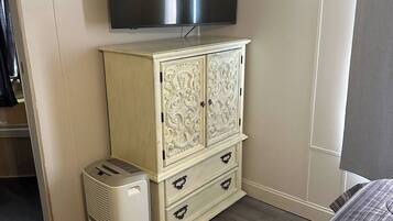 A bedroom with a bed, a TV mounted on the wall, a wardrobe, and a heater.
