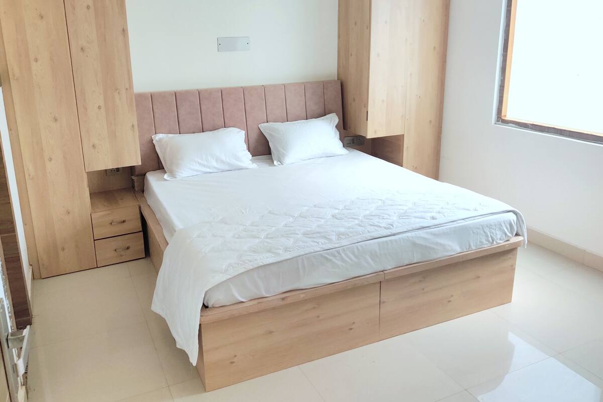 A bedroom with a wooden bed frame, two white pillows, and a wooden wardrobe.