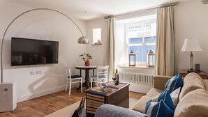 A cozy living room with a flat-screen TV, a sofa, a coffee table, and a dining area with chairs and a small table. - The Pilchard Press, The Pilchard Press on Harbourside in Mevagissey Village with FREE Parking (Saint Austell)