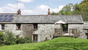 A stone house with solar panels, a chimney, and a small patio with a table and chairs. - The Barn - Two Bedroom Cottage, Sleeps 4 (Camelford)