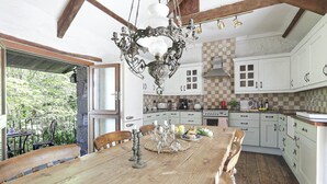 A rustic kitchen with wooden beams, white cabinets, and a large wooden dining table set for a meal. - The Barn - Two Bedroom Cottage, Sleeps 4 (Camelford)