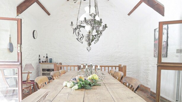 A rustic dining room with a large wooden table, a chandelier, and a view of the outdoors. - The Barn - Two Bedroom Cottage, Sleeps 4 (Camelford)