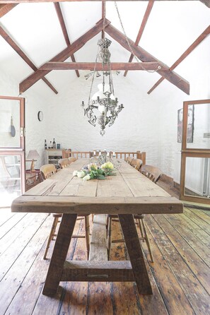 A rustic dining room with a large wooden table, a chandelier, and a view of the outdoors. - The Barn - Two Bedroom Cottage, Sleeps 4 (Camelford)