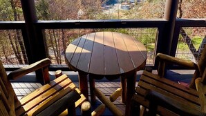 A wooden deck with a round table and two chairs, overlooking a valley with autumn foliage and distant mountains.