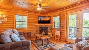 A cozy log cabin interior with a fireplace, comfortable seating, and a television.
