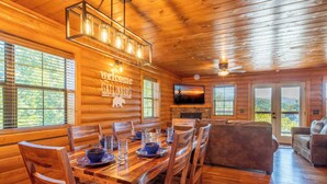 A wooden cabin interior with a dining area, a fireplace, and a sofa.
